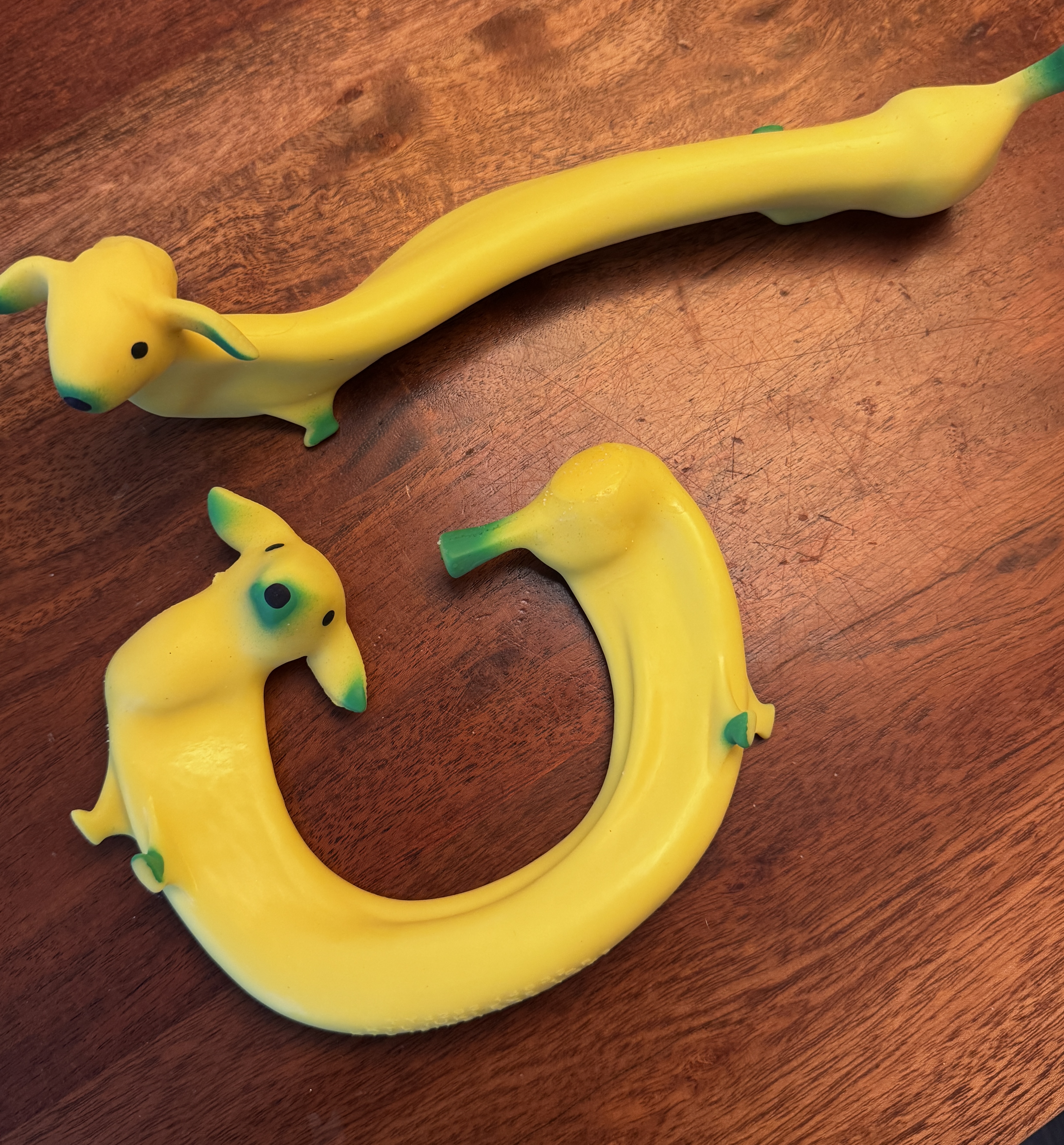Two soft, stretchy sand-filled banana dog toys; yellow banana-shaped bodies with little dog faces, sitting side by side.