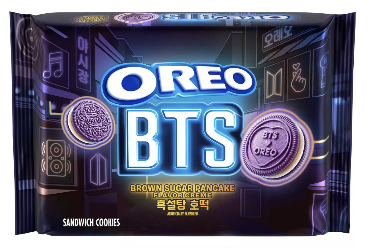 A purple package of brown sugar pancake oreos, with the blue OREO logo and bold BTS lettering over a neon cityscape, two cream-filled chocolate cookies pictured at the bottom and Korean lettering for the brown sugar pancake flavor.