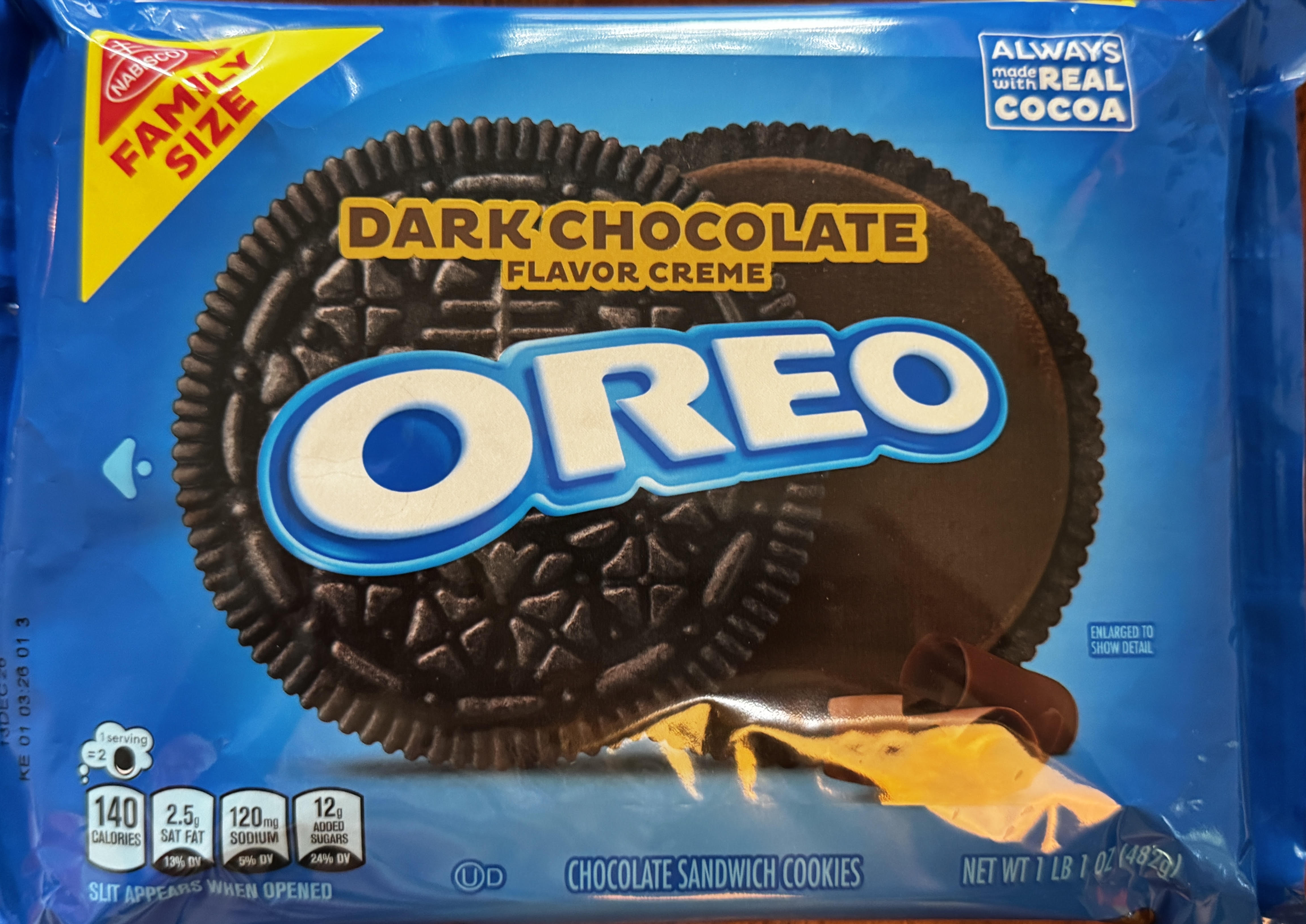 A blue Nabisco Family Size OREO package labeled 'Dark Chocolate Flavor Creme,' with a large chocolate sandwich cookie graphic, a 'Made with Real Cocoa' badge, chocolate curls, and text reading 'Chocolate Sandwich Cookies, Net Wt 1 lb 1 oz.'