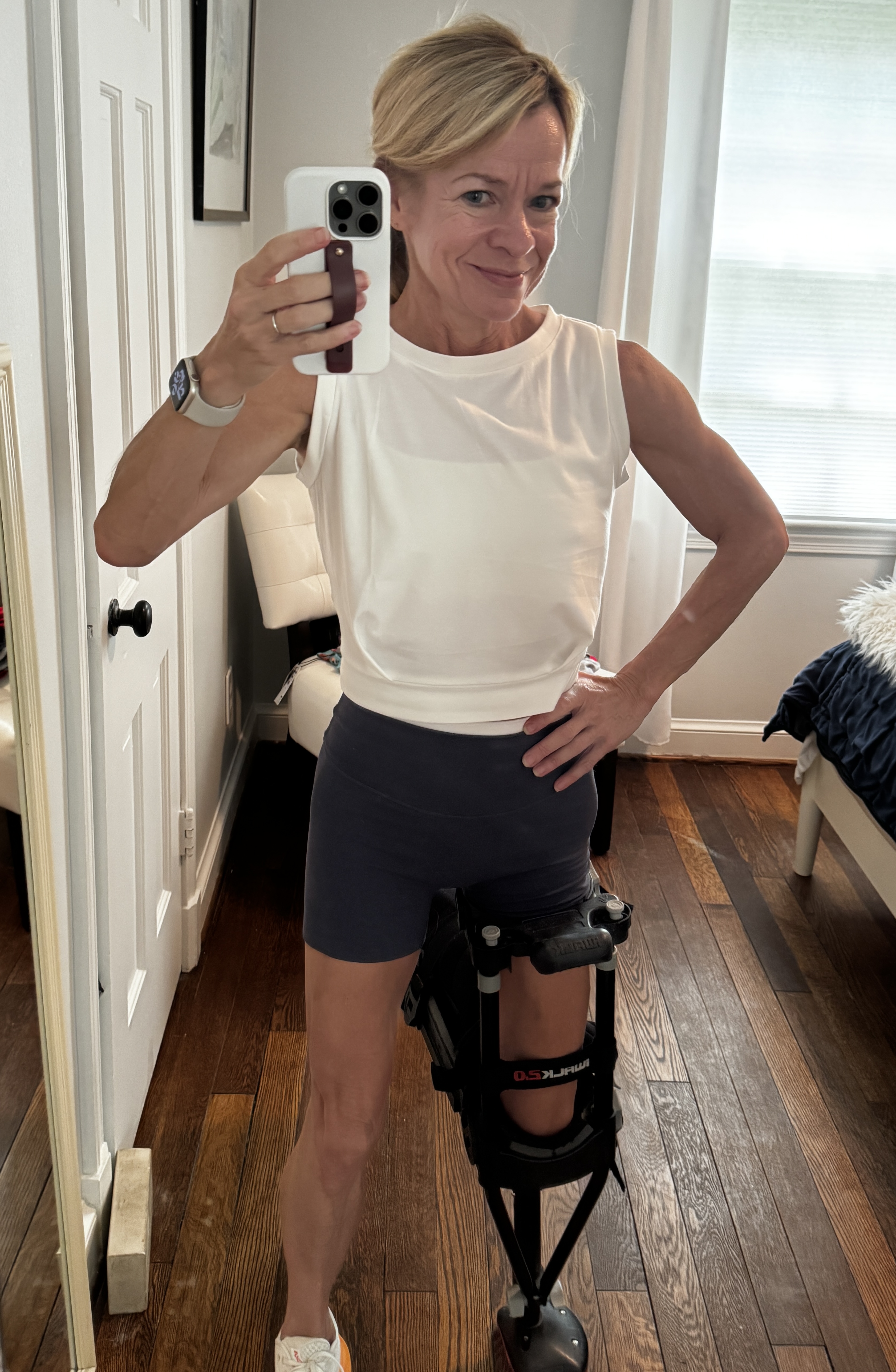 Mirror selfie in my gym clothes, right leg strapped into the iWalk, flexing just enough to prove the hips-and-up clearance is being taken very seriously.